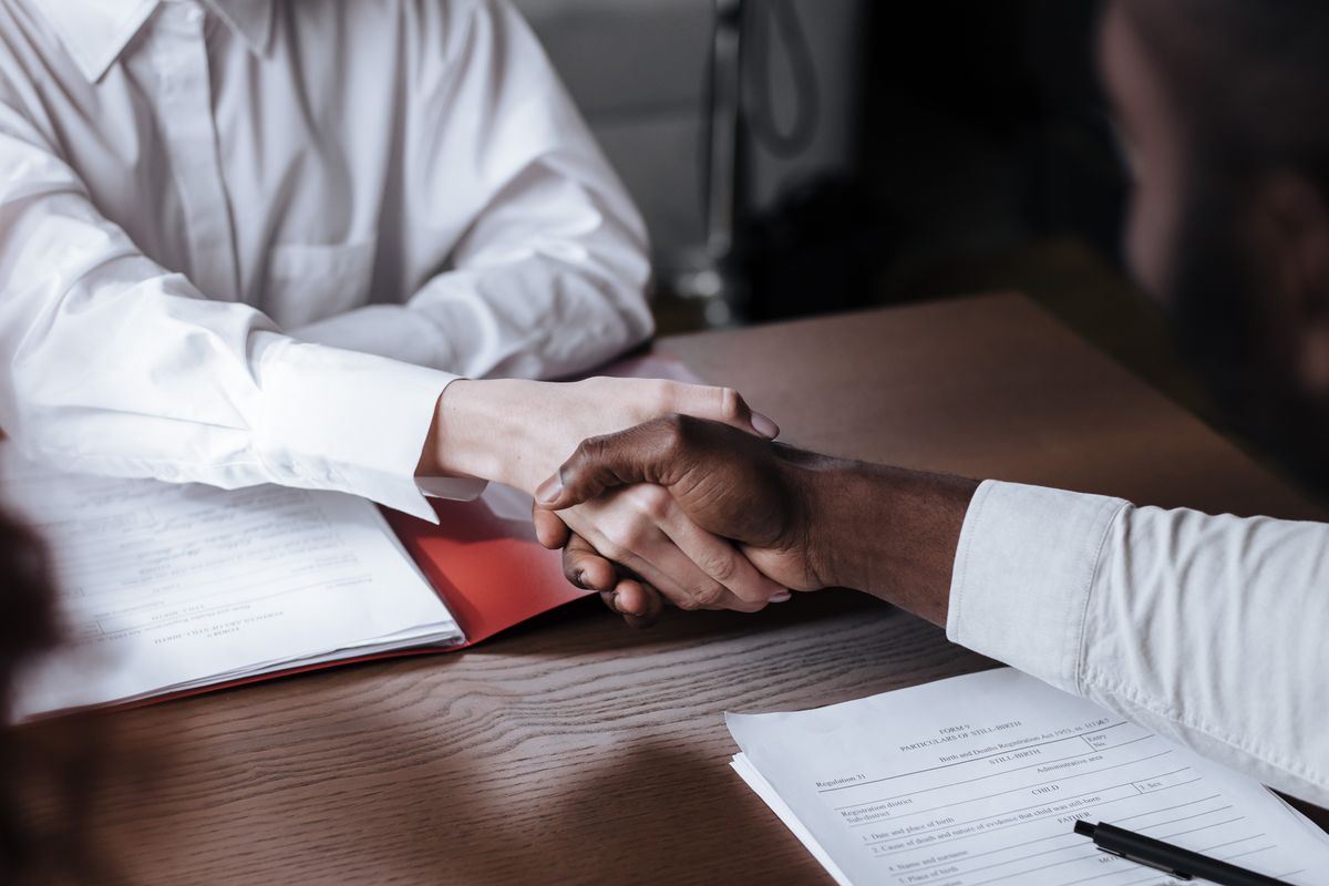 Two people shaking hands over signed service agreement documents