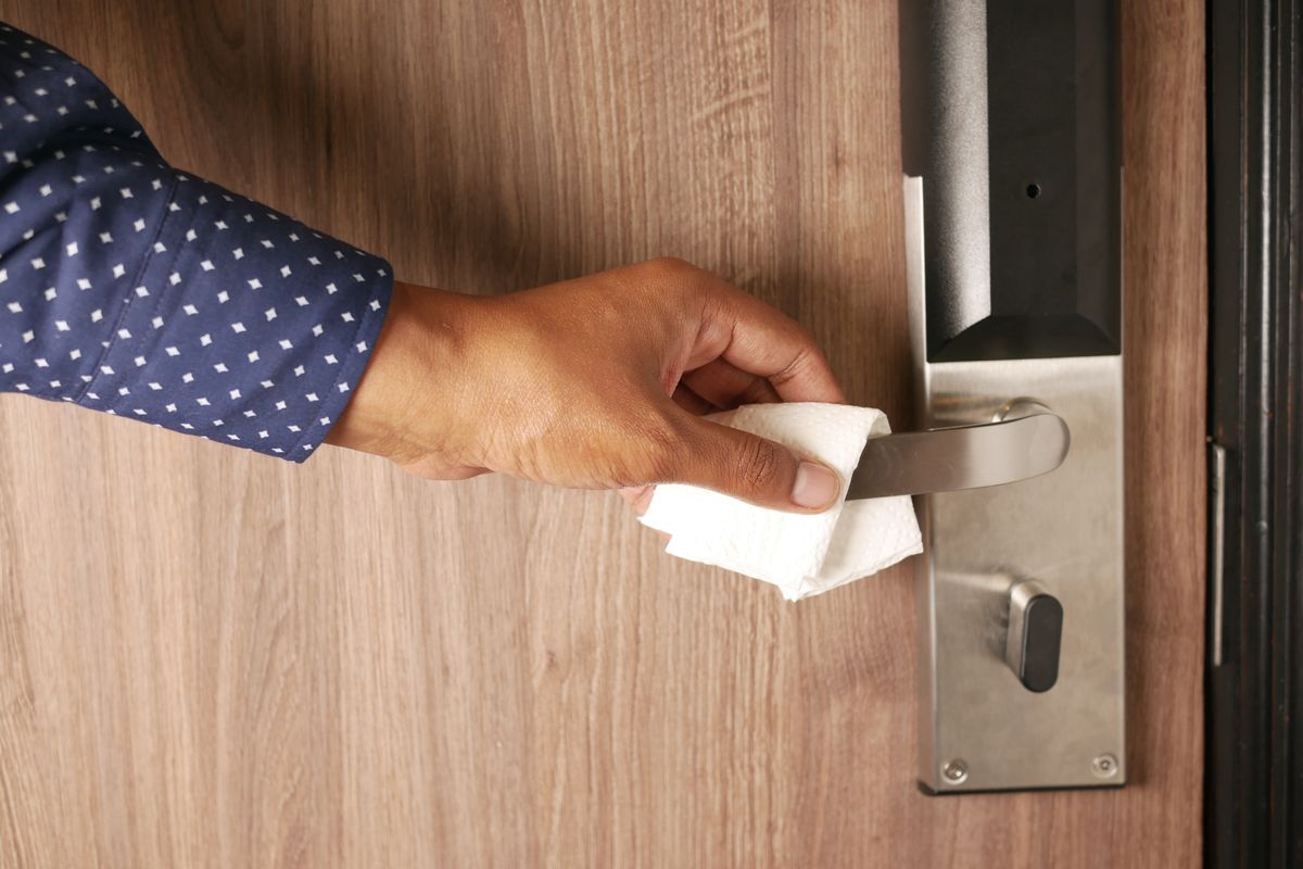 Hand wiping a metal door handle with a paper towel